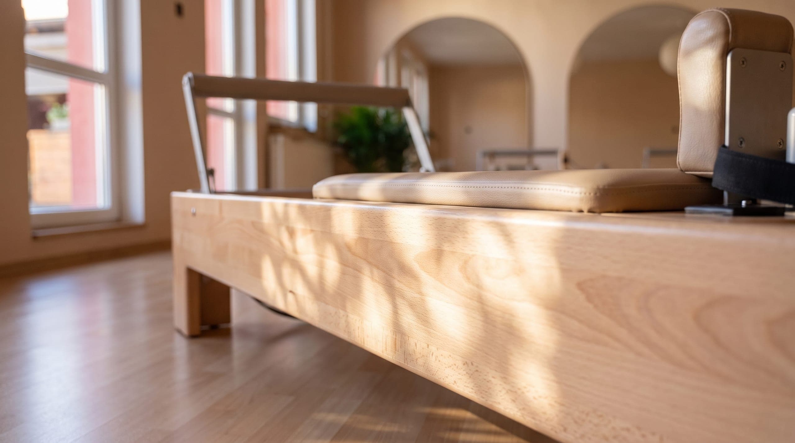 Detail dřevěného Pilates Reformeru s čalouněným vozíkem v ranním světle